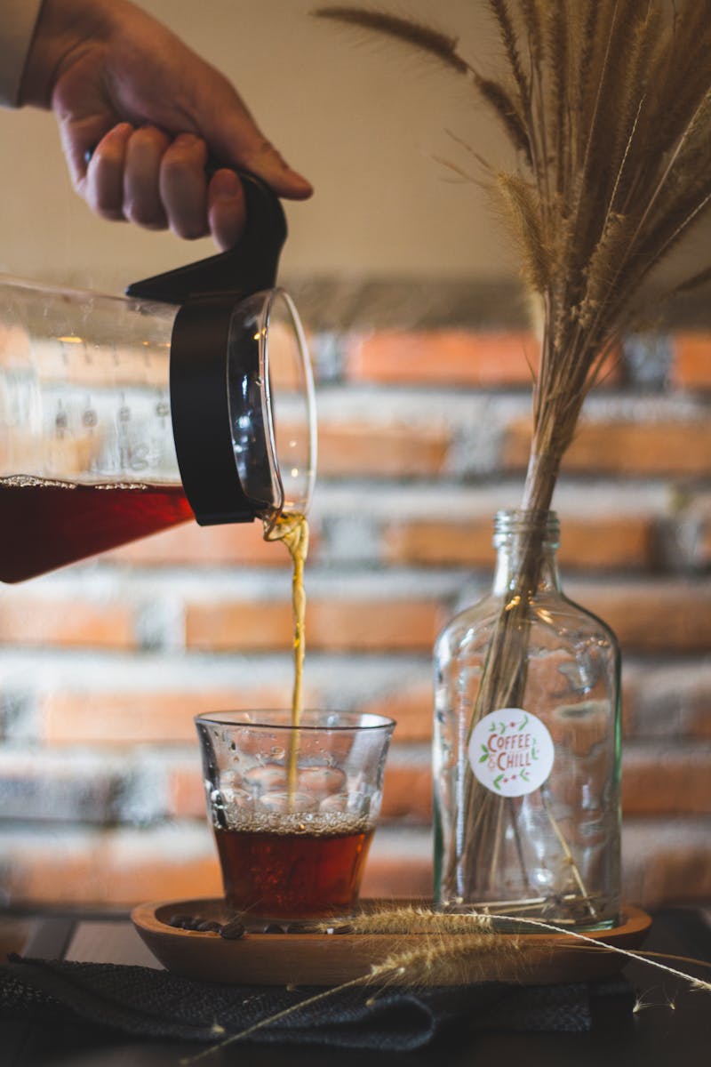 Person Pouring Brown Liquid on Clear Glass